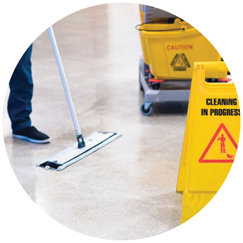 A custodian mopping the floor with cleaning cart and caution sign on