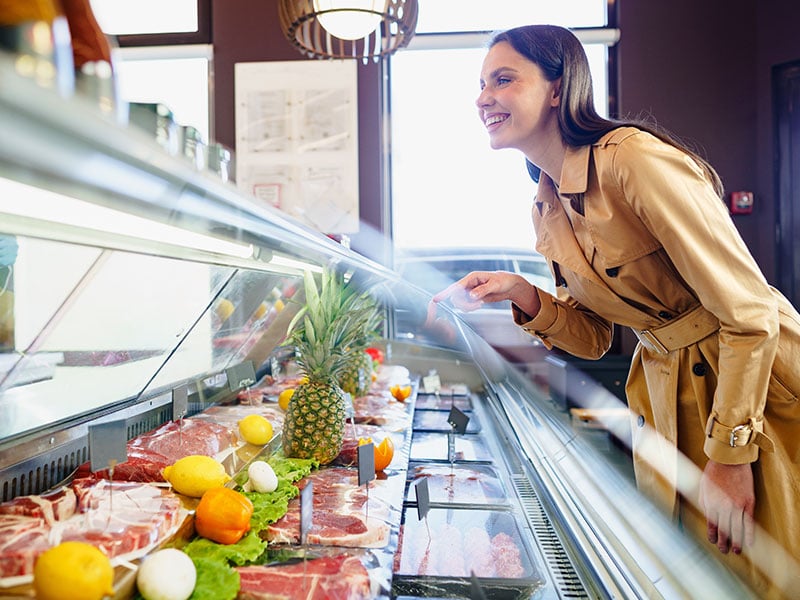 a young happy female customer purchasing packaged meat at the grocery store-supermarket solutions