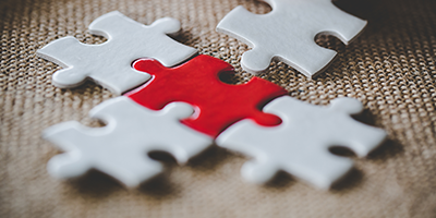 An image of puzzle pieces one being red getting fitted together