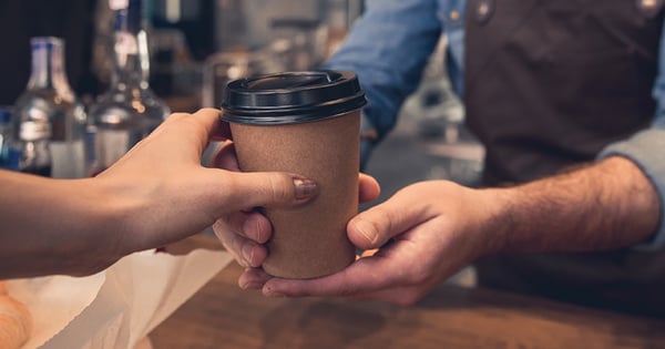A foodservice staff handing coffee in a disposable cup to a customer over the counter