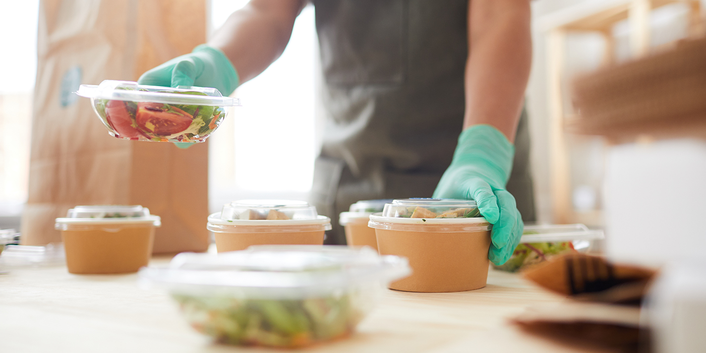 Foodservice worker with gloves preparing eco-friendly disposables. 
