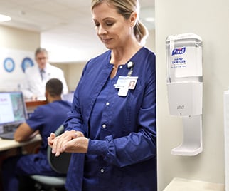 a healthcare worker using wall mounted PURELL hand sanitizer dispenser