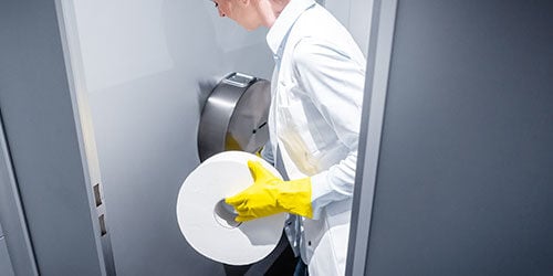 Building maintenance person replacing jumbo roll of commercial toilet paper