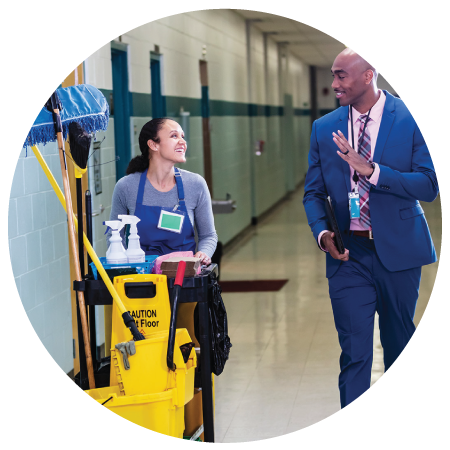 a school custodian pulling her cleaning cart while talking to a school staff in a hallway