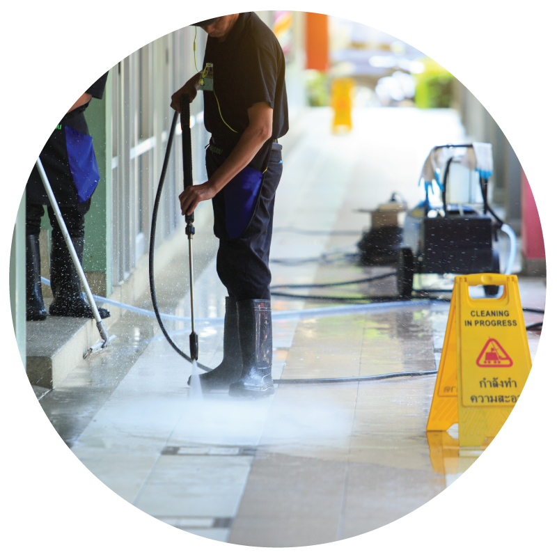 A janitor power washing building front with wet floor sign