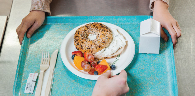 a student carrying a tray of lunch with bagel