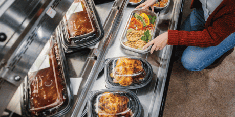 A woman picking out ready meal kit in a disposable container at the grocery store hot bar