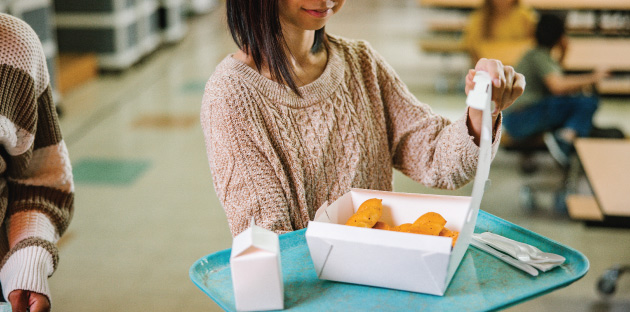 A student carrying a tray with disposable box container with food