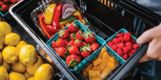 womans hand picking up fruit in grocery store produce section and putting it in basket