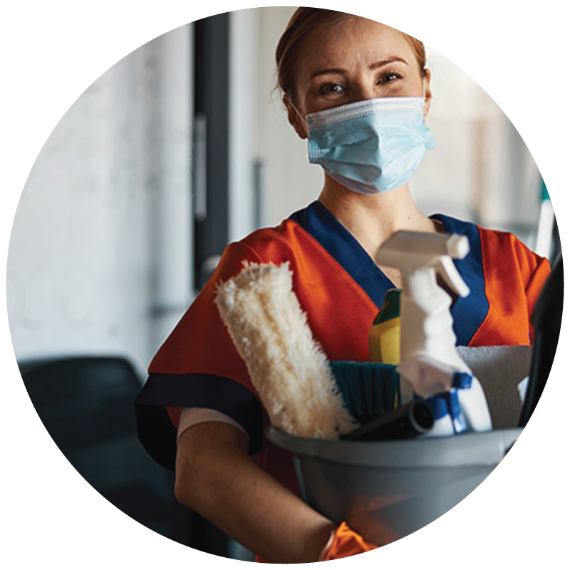 A janitor holding a bucket full of cleaning supplies, wearing a mask