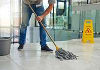 custodian mopping the floor with wet floor sign nearby