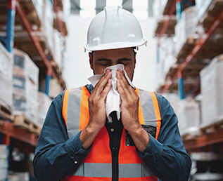 a warehouse worker blowing nose with a tissue for cold, flu