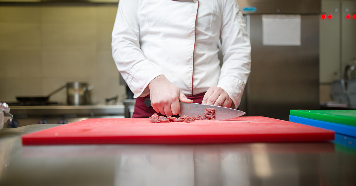 A chef cutting mean using color-coded cutting board for food safety