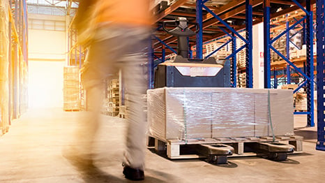 A warehouse worker walking by palletized shipment in a warehouse