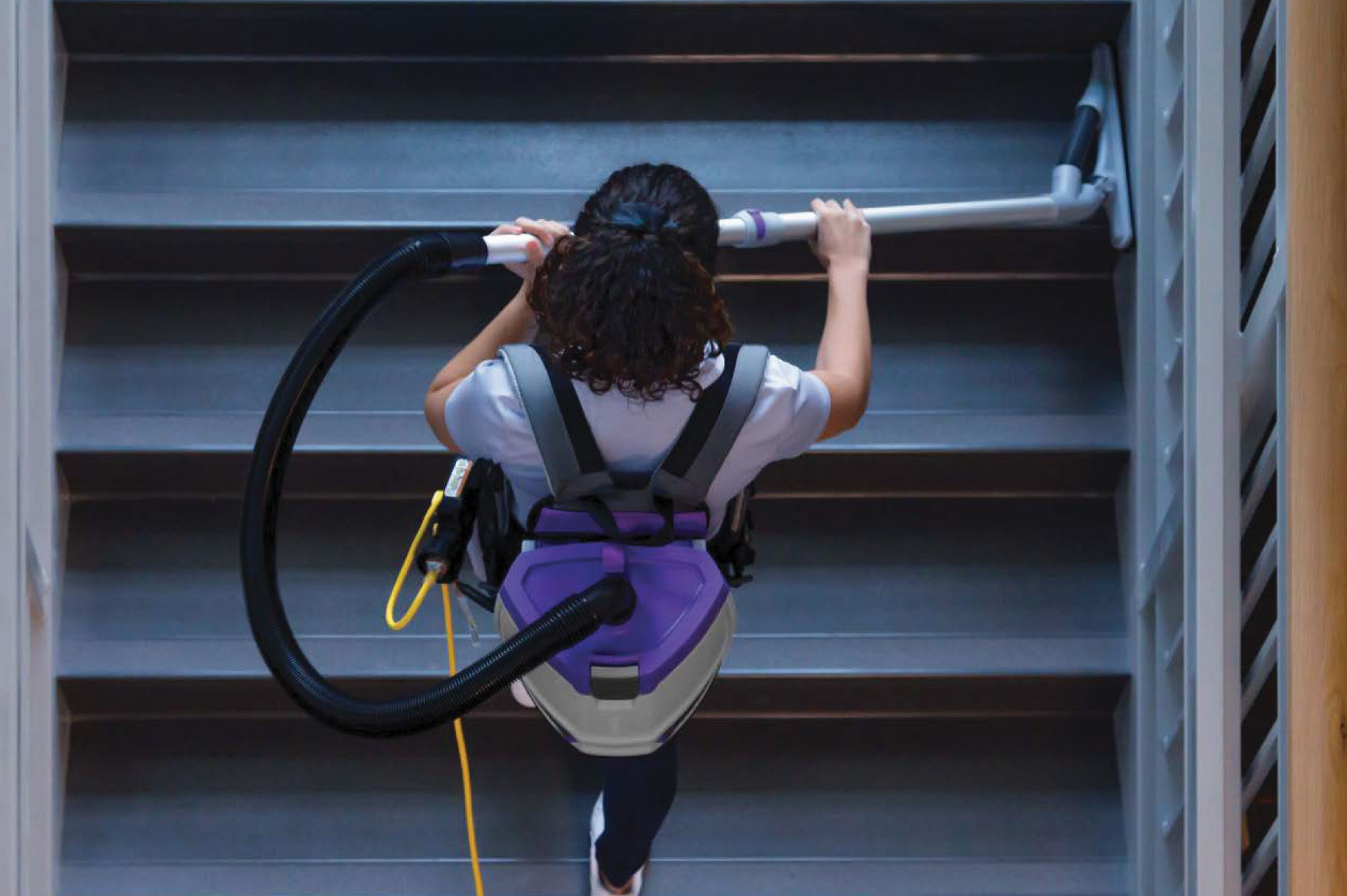a janitor using ProTeam backpack vacuum on a staircase